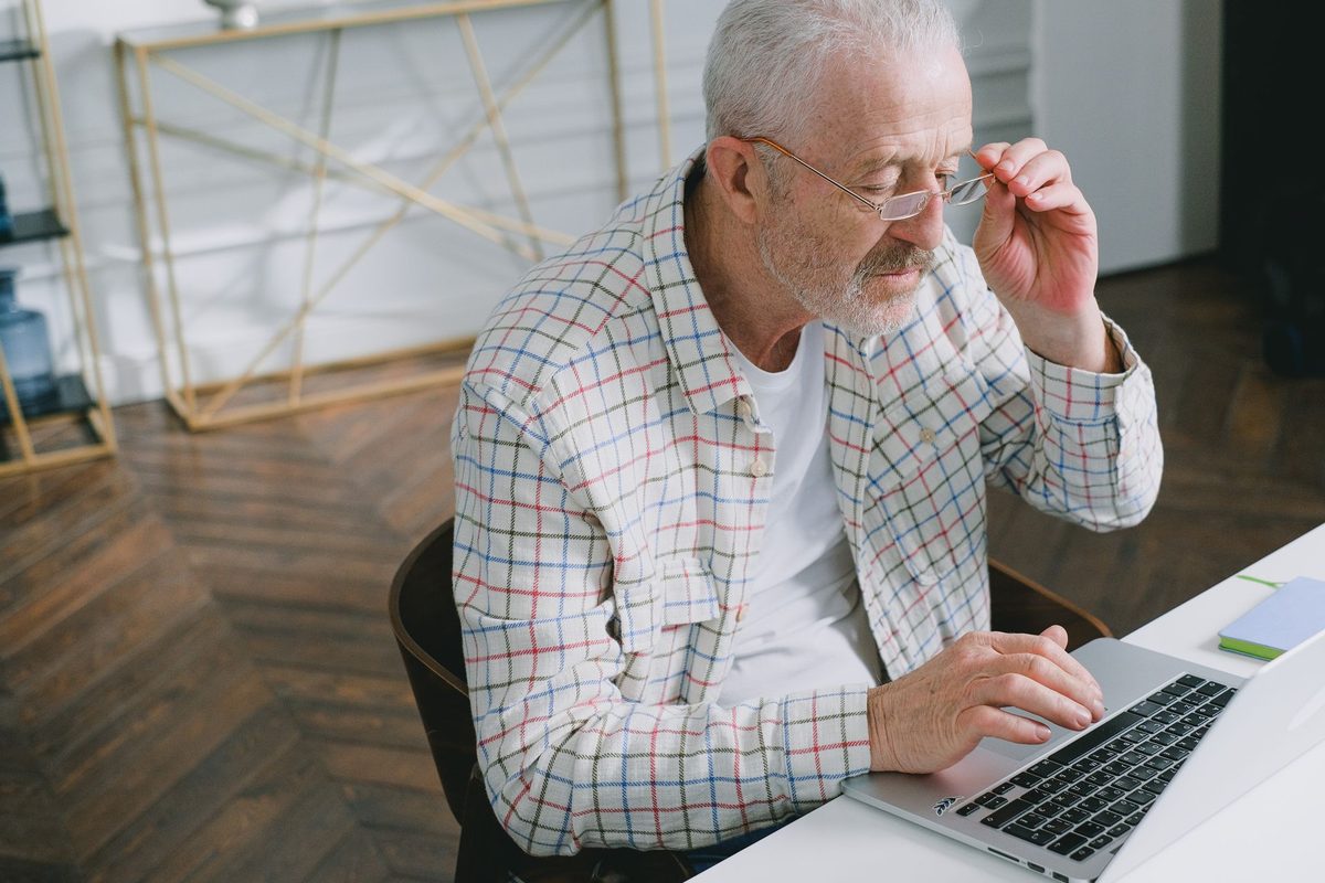 A grey-haired man with glasses thinking at his laptop